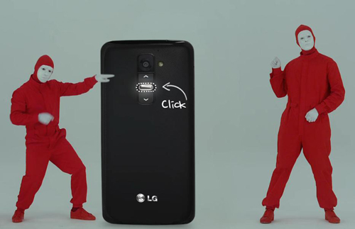 A wallpaper of the Play & Share LG G2 campaign – a back view of a gigantic LG G2 between two men wearing red body suits.